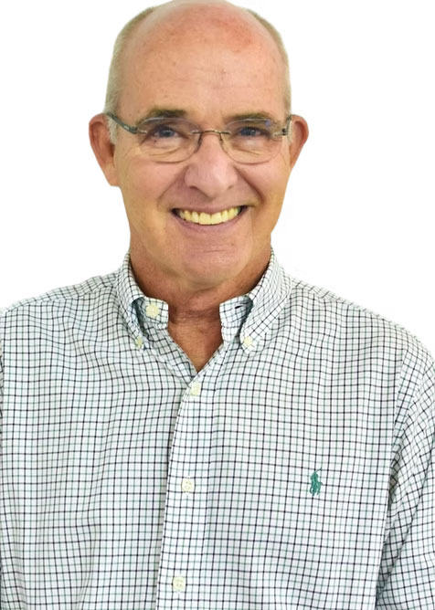 The image shows a man wearing glasses, with gray hair, smiling at the camera, dressed in a checkered shirt and a patterned tie, standing against a white background.