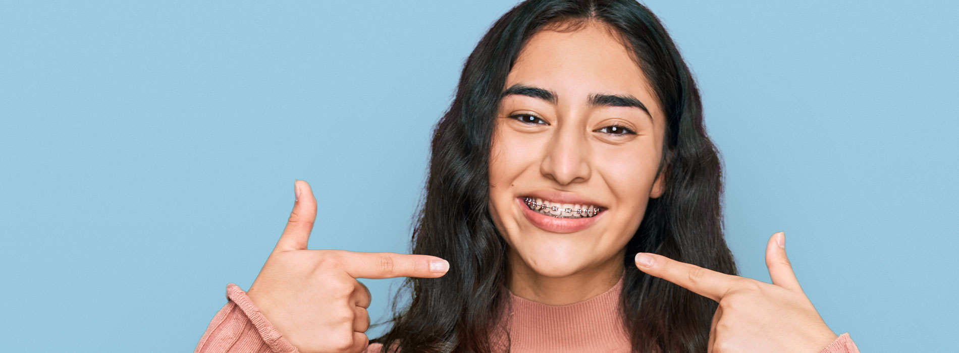 The image shows a person making a peace sign with their hands while smiling at the camera against a blue background.