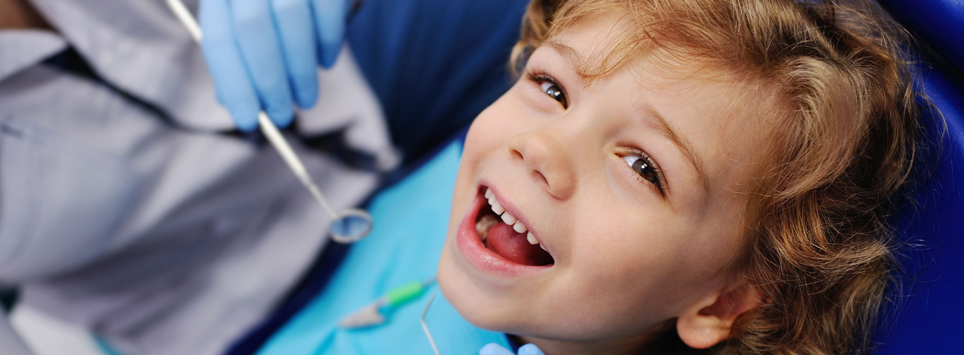 Baby with toothy smile looking at camera while receiving dental care.
