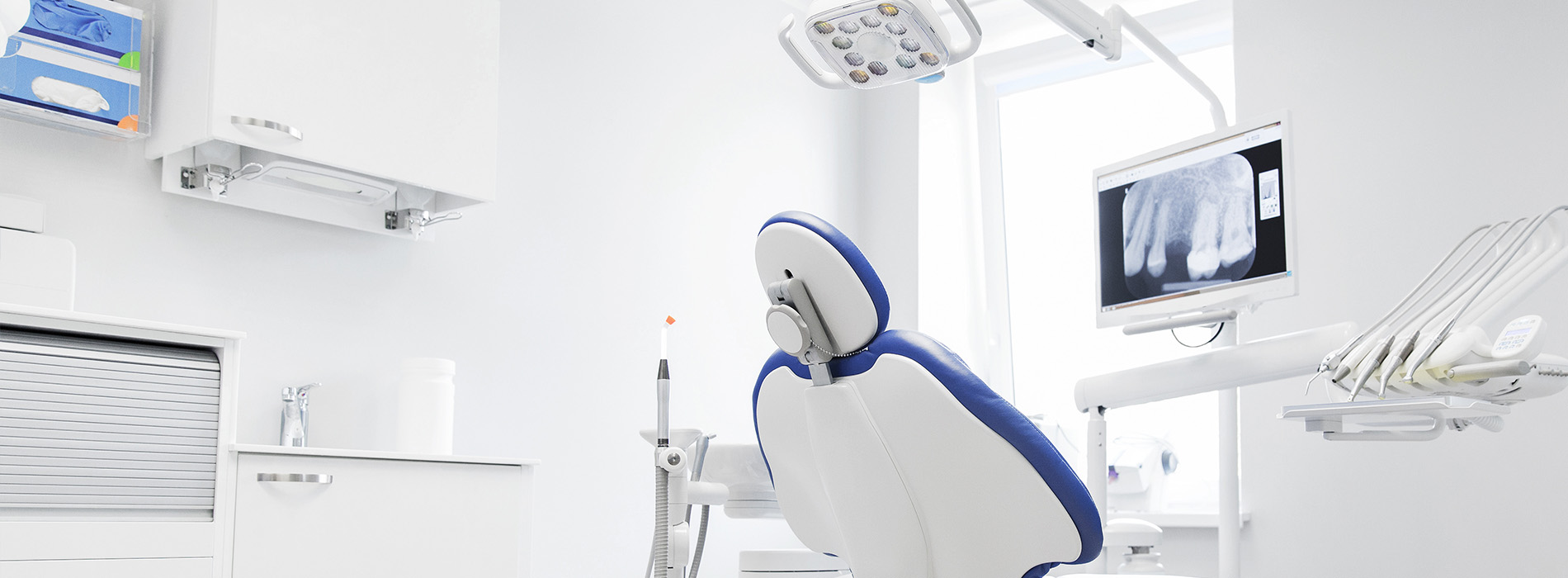 The image shows a modern dental clinic with a blue chair, equipment, and a clean, white interior.