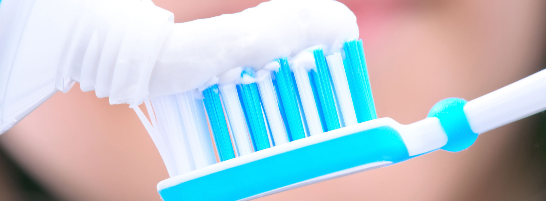 An electric toothbrush with blue bristles being held up against a person s face, set against a blurred background.