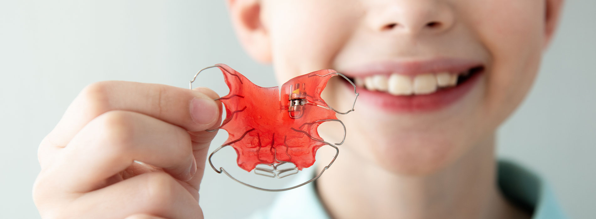 The image shows a young child holding up a small red object with a smile on their face.
