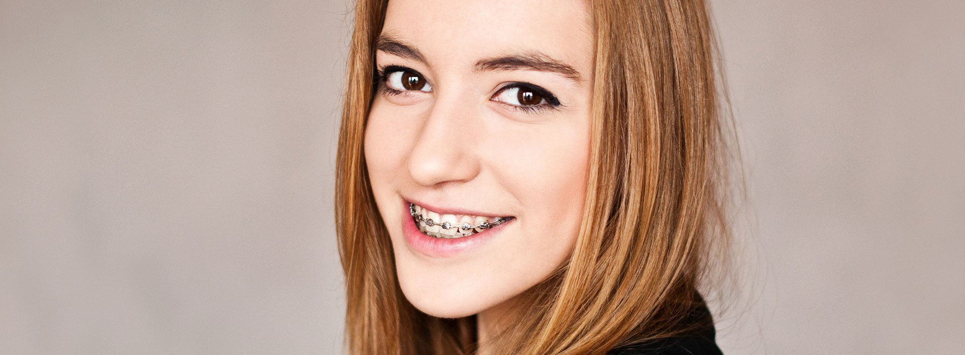 The image shows a young woman with red hair, wearing makeup, looking directly at the camera with a slight smile. She has a fair complexion and is set against a plain background.