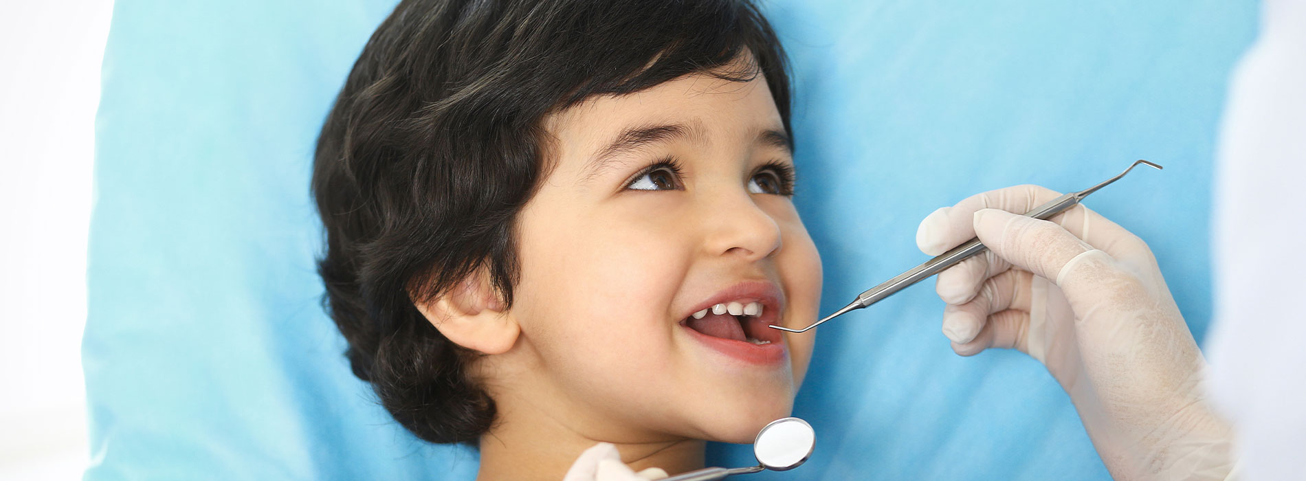 A young child receiving dental care with a dentist using a tool to examine their teeth.