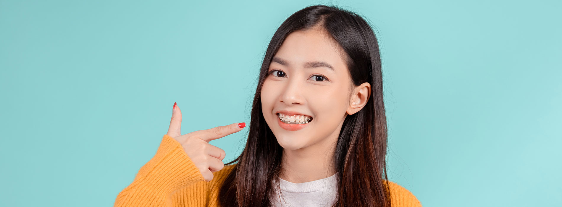 A young woman with red nail polish gesturing with her right hand while smiling and pointing towards the camera.