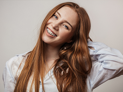 A young woman with long red hair poses confidently, smiling gently and leaning slightly forward, against a white background.